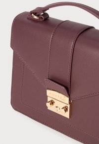 Sac à main en simili cuir mauve avec un design structuré, quincaillerie dorée et fermeture à cliquet. Présente des accents cousus sur le corps.