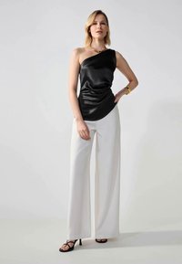 Black satin one-shoulder top with draped design, paired with white wide-leg pants and strappy black heels. Simple gold jewelry accents.