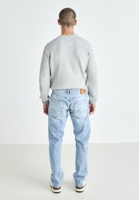 Grå ribbestrikket genser med rund hals, kombinert med lyseblå rette jeans med baklommer og et lærmerke på livet.