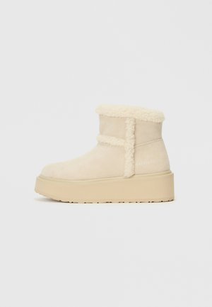 Stivale alla caviglia in suede beige con un colletto morbido color crema, suola piatta e logo "Valentino" in rilievo di lato.