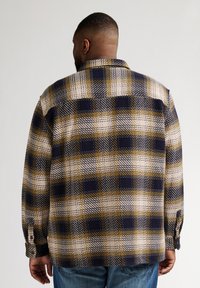 Camicia di flanella a maniche lunghe con un motivo a quadri nei colori blu navy, oro e crema. Realizzata in un tessuto testurizzato con polsini bottonati.
