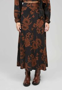 Jupe midi à motifs floraux marron en tissu léger, au design fluide, associée à des bottes chevilles marron.