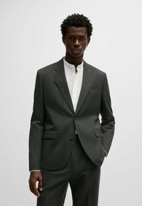 Abito grigio con un motivo, chiusura a due bottoni, tasche a patta e revers a punta, abbinato a una camicia bianca con colletto sotto.