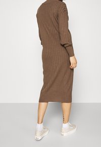 Brun ribbat stickad klänning med långa ärmar och krage, som når till halva vaden. Till detta matchade vita strumpor och ljusa sneakers.