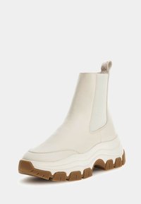 Stivale Chelsea crema in pelle liscia con pannelli laterali elastici, coulisse e suola in gomma spessa e testurizzata di colore marrone chiaro.