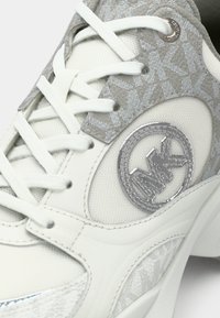 Λευκό αθλητικό παπούτσι με υφή γκρι μοτίβου, στρογγυλό λογότυπο και επίπεδα κορδόνια. Διαθέτει λείο, γυαλιστερό στοιχείο στο πλάι.