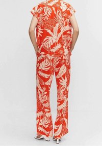 Completo a due pezzi con motivo floreale in un vivace rosso, decorato con grandi foglie tropicali bianche. Top largo e pantaloni a gamba larga. Tessuto dalla consistenza liscia.
