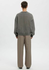 Grauer Strickpullover mit Rundhalsausschnitt, überschnittenen Schultern und geripptem Saum, kombiniert mit beigen, weit geschnittenen Hosen und schwarzen Schuhen.