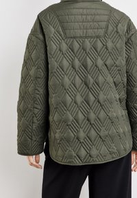 Giacca trapuntata di colore verde oliva, con un motivo a diamante con dettagli in rilievo, vestibilità rilassata, maniche lunghe e orlo leggermente arrotondato.