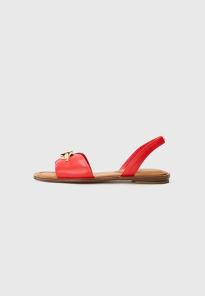 Rød læder flad sandal med åben tå, rem bagpå, guldfarvet spænde detalje og tanfarvet sål på en lys grå baggrund.