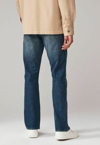 Jeans de culoare albastră închisă cu o croială dreaptă clasică, fabricate din denim. Asortați cu o cămașă bej cu mânecă lungă și adidași albi.