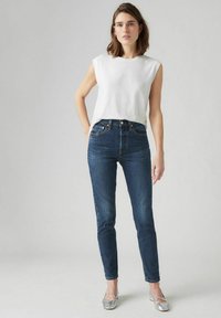 Witte mouwloze top, hooghogere donkerblauwe jeans en zilveren ballerina's; gladde stof, slim fit en klassieke silhouet.