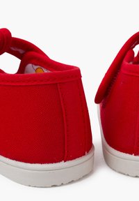 Scarpe di tela rosse con retro arrotondato, chiusura a elastico e suole in gomma bianche. L'interno presenta una fodera colorata a motivi.