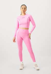 Różowy sportowy top crop i legginsy z wysokim stanem, z kontrastującymi ciemnymi szwami. Miękki, elastyczny materiał z dopasowanym krojem.