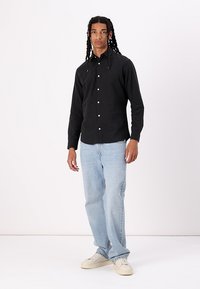 Svart skjorte med knapper, lange ermer, laget av bomull. Kombinert med lyseblå, rette jeans og hvite joggesko. Enkel, strukturert design.