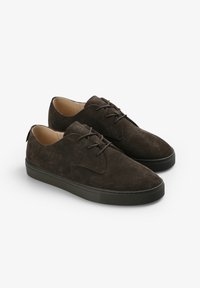 Zapatos de ante marrón con cordones, puntera redondeada, suela de goma texturizada en contraste y diseño minimalista.