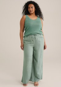 Top sin mangas de color verde texturizado con tirantes anchos, combinado con pantalones holgados de color verde claro que cuentan con una cintura elástica y cordón.