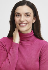 Pull en col roulé ajusté de couleur rose vif, fabriqué en tissu tricoté doux. Il présente des manches longues et un col côtelé avec une texture lisse.