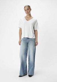 Camiseta blanca de cuello en V con mangas cortas, combinada con jeans de mezclilla de pierna ancha azul claro y botas negras de tacón. Tejido suave y ajuste relajado.