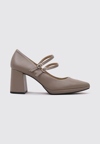 Chaussure beige à talons blocs avec un bout pointu et deux brides de cheville, fabriquée en matériau synthétique lisse. Présente des détails de couture subtils.