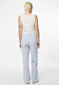 Witte mouwloze top met een gestructureerde afwerking, gecombineerd met lichtblauwe en witte gestreepte flared broek met een elastische tailleband.