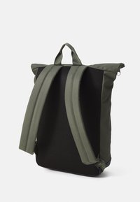 Olive green backpack with a textured mesh back, dual straps, and a top handle. Features a foldable design for compact storage.