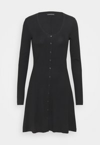 Robe pull noire côtelée avec manches longues, décolleté en scoop et fermeture à boutons sur le devant. Présente un ourlet évasé.