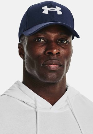 Marineblå baseballcap med et hvidt Under Armour-logo, med en struktureret design og buet skygge, båret med en hvid hættetrøje.
