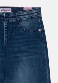 Tumedad sinised laiad teksad sileda denimitekstuuriga, eest taskud ja väike hõbedane nupude detail. Omab brändi ja tooteetikette.