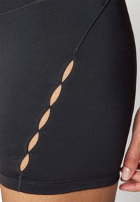 Černé šortky z elastické látky s bočními výřezy ve tvaru oválu a vodorovným prošíváním podél lemu.