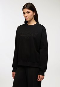 Felpa nera con polsini a costine, scollatura rotonda e "SELFLOVE Club" embosso al centro. Realizzata in un morbido tessuto testurizzato.