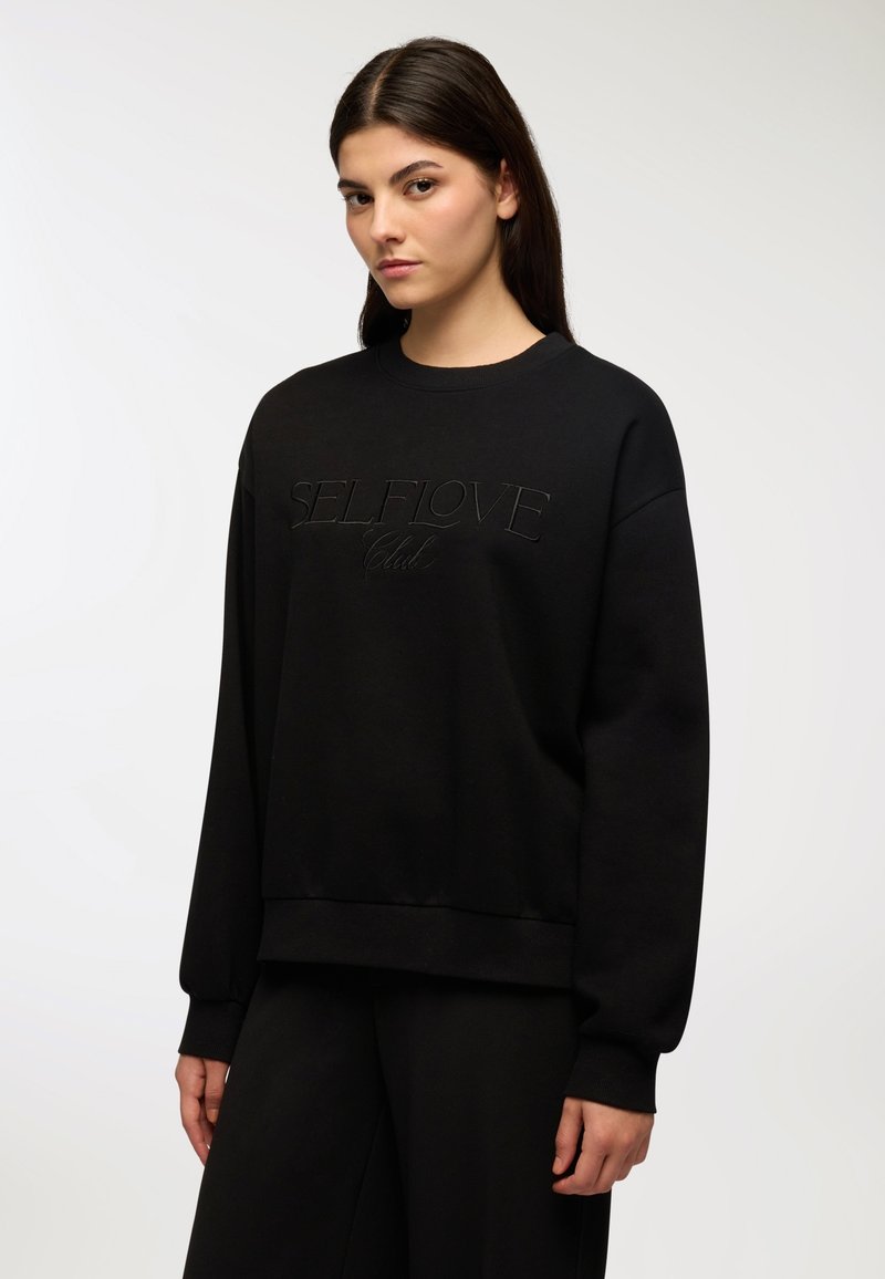 Felpa nera con polsini a costine, scollatura rotonda e "SELFLOVE Club" embosso al centro. Realizzata in un morbido tessuto testurizzato.