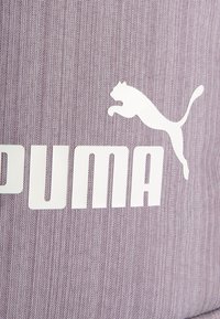 Tissu texturé violet avec un logo PUMA blanc bien en vue et une silhouette de puma sautant. Design épuré avec des couleurs contrastées.
