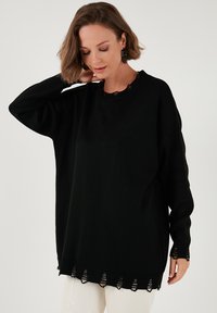 Pulover negru supradimensionat cu un guler cu nervuri și un tiv detaliat, având accente tăiate. Textură moale, croială lejeră și mâneci lungi.