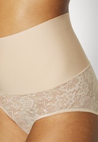 Beige magas derekú alsónemű sima elasztikus derékpánttal és finom virágmintás csipkével, mely bonyolult mintákkal díszíti az éleket.