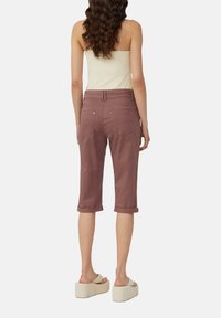 Bordowe spodnie 3/4 z mankietami, z tylnymi kieszeniami i gładką teksturą materiału. Noszone z beżową bluzką i jasnym obuwiem.