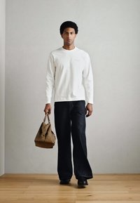 Balta krekla ar garām piedurknēm, tumši platām džinsu biksēm un brūnu somu. Audums šķiet mīksts; somai ir teksturēts virspusējums un plecu siksna.