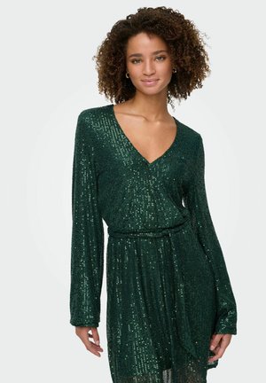 Robe en sequins verts avec un décolleté en V plongeant et des manches longues. Le tissu est texturé avec des sequins brillants et présente une ceinture en tissu à la taille.