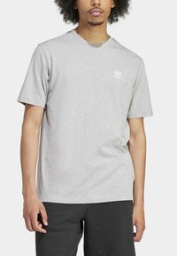 Šedé bavlněné tričko s krátkým rukávem a kulatým výstřihem, s bílým logem adidas na levé části hrudi. Hladká textura, standardní střih.