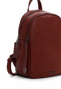 Sac à dos en cuir rouge avec une forme arrondie, deux compartiments zippés, une surface texturée, des accents cloutés et un détail de logo métallique.