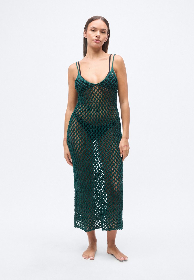 Πλεκτό φόρεμα-επένδυση σε πράσινο χρώμα με μοτίβ ο διαμαντένιου πλέγματος, λαιμόκοψη scoop και λεπτές τιράντες, που φτάνει μέχρι τη μέση της γάμπας. Το μοντέλο είναι ξυπόλυτο και στέκεται όρθιο.