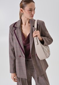 Beige handtas met een gewatteerd patroon en gouden hardware, gecombineerd met een geblokte bruine blazer en een bordeauxrood top, met een ontspannen pasvorm.