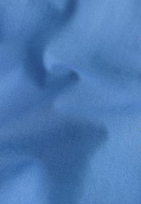 Gros plan sur un tissu bleu à texture côtelée fine et pliures subtiles créant des ombres douces.