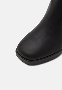 Svart ankelboot med rund tå, slätt konstläder, låg klack och utan dekorationer. Har en elegant, minimalistisk design.