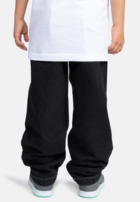 Pantalones de mezclilla negros con un ajuste relajado, con dobladillo vuelto, combinados con zapatillas grises y una camiseta blanca lisa.