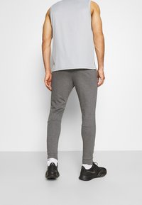 Grå ärmlös sporttopp tillsammans med åtsittande grå byxor, som visar en slät textur och avsmalnande design, kompletterat med svarta sneakers.