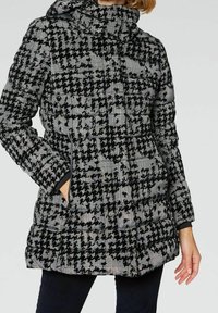 Pikowany płaszcz w czarno-białą kratę, z wysokim kołnierzem, dwoma bocznymi kieszeniami oraz pikowaną fakturą.