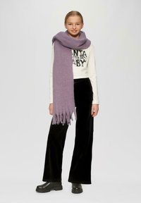 Paarse, franjesjaal gemaakt van zachte wol, gedragen over een wit langemouwen shirt met een grafisch ontwerp, gecombineerd met zwarte fluwelen broek en laarzen.