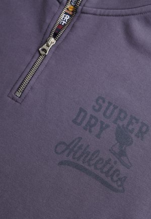 Purple zip-up sweatshirt with a silver zipper. Features "SUPER DRY Athletics" printed in dark gray across the chest. Soft fabric texture.