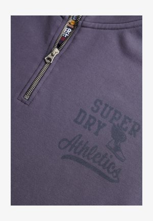 Fioletowa bluza z suwakiem z metalowym zamkiem. Na piersi nadruk "SUPER DRY Athletics" w ciemnoszarym kolorze. Miękka faktura tkaniny.